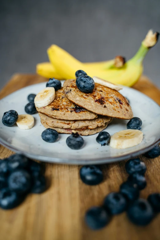 a white plate topped with pancakes and blueberries, banana, 120mm, speckled, oak