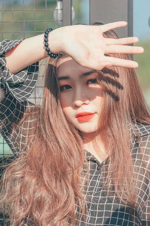 a woman standing in front of a fence with her hands on her head, a picture, inspired by Kim Jeong-hui, trending on pexels, light-red lips, square, ulzzang, brown long hair