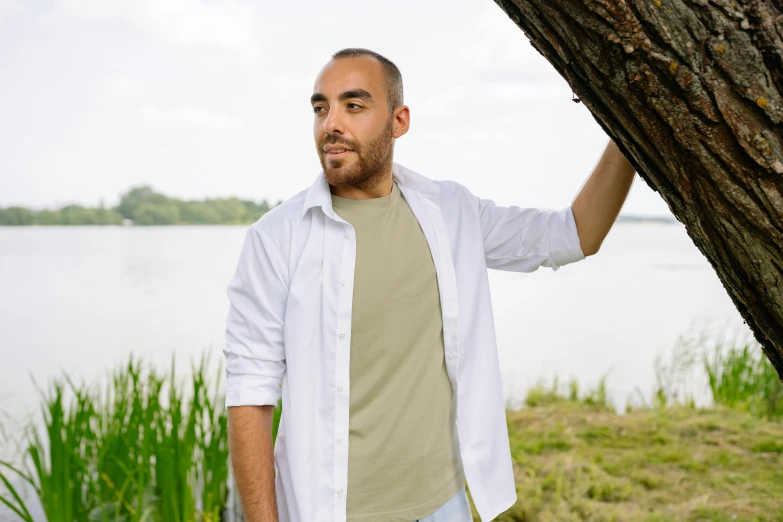 a man wearing a white shirt stands under a tree next to water