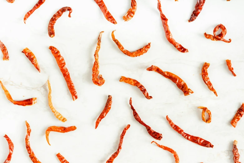 a pile of dried chili sitting on top of a counter, by Carey Morris, trending on pexels, white and orange, scorpion tail, solid background, background image