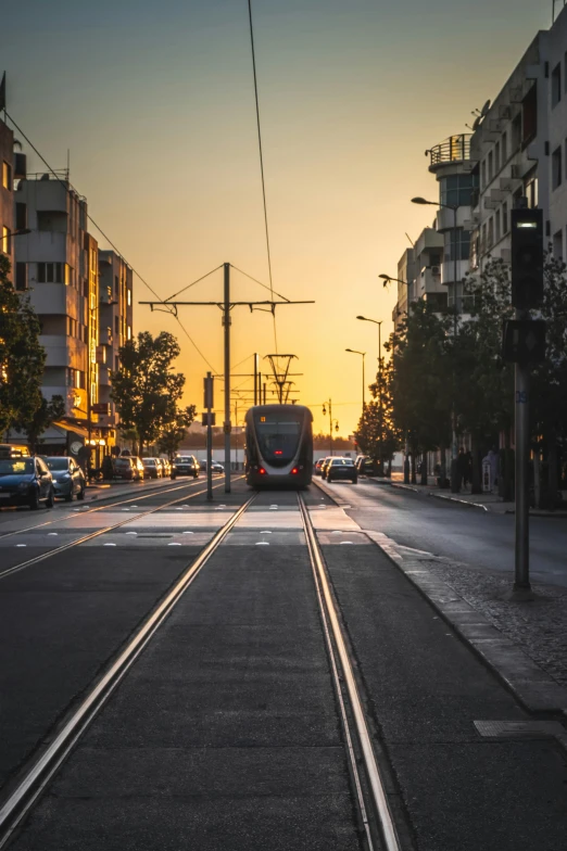 a train traveling down a street next to tall buildings, by Niko Henrichon, pexels contest winner, happening, israel, sunrise lighting, square, tram