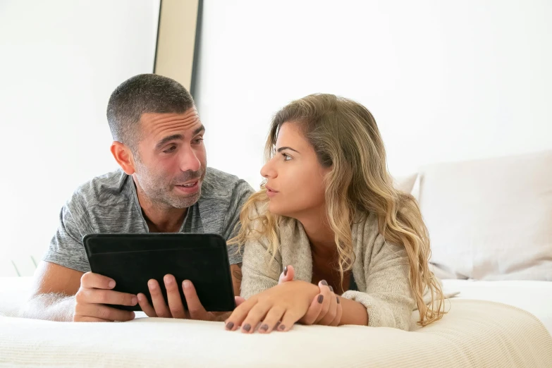 a man and a woman laying on a bed looking at a tablet, pexels contest winner, spanish, looking to the right, raphael lecoste, profile image