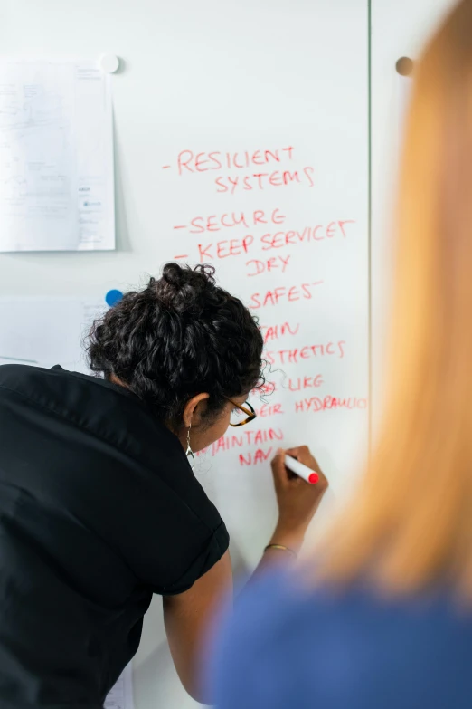 a woman writing on a whiteboard in a classroom, by Arabella Rankin, in a meeting room, programming, environmental shot, maintenance photo