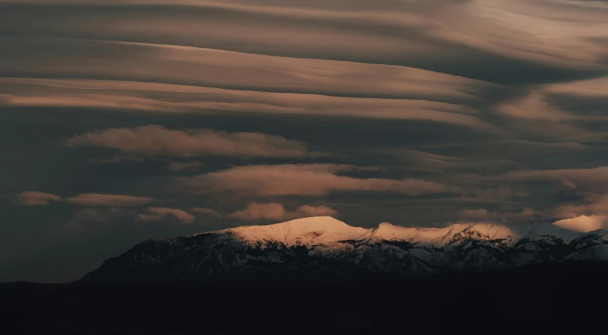 the top of a snowy mountain is in the foreground with some clouds above