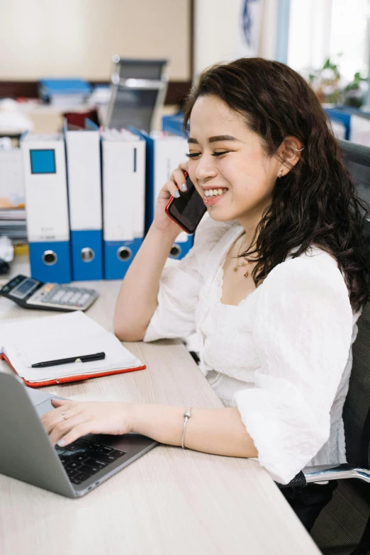a woman sitting at a desk talking on a cell phone, inspired by Ruth Jên, trending on pexels, asian decent, smiling slightly, in an call centre office, white