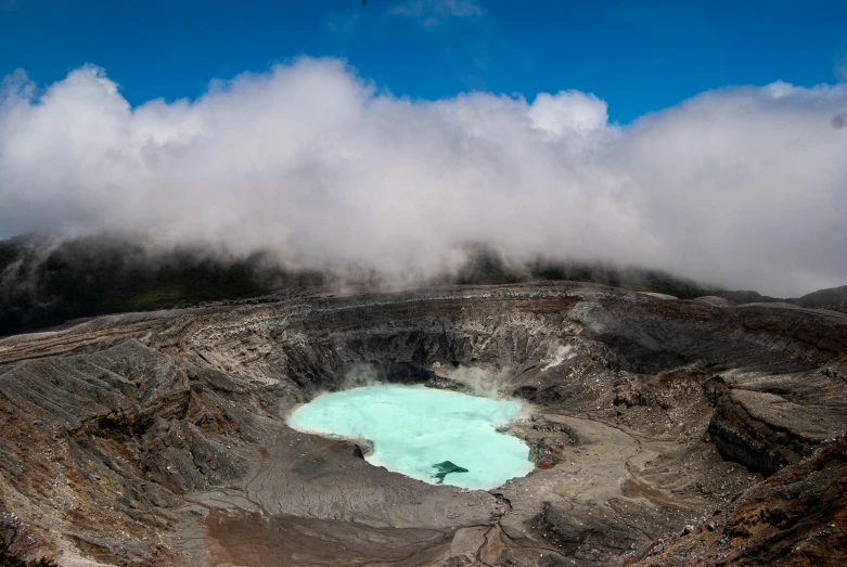 a blue pond in the middle of a large crater with clouds