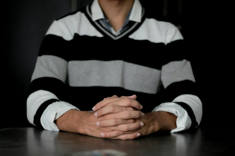 a man sitting at a table with his hands folded, unsplash, striped sweater, taken in the late 2010s, white sleeves, holding court