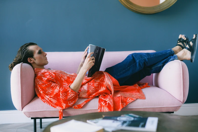 a woman laying on a couch reading a book, by Alice Mason, wearing fuchsia silk robe, wearing double denim, orange jumpsuit, wearing a luxurious silk robe