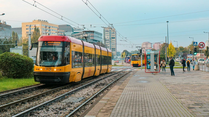 a yellow and red train traveling down train tracks, by Adam Marczyński, pexels contest winner, street tram, panoramic, square, grey