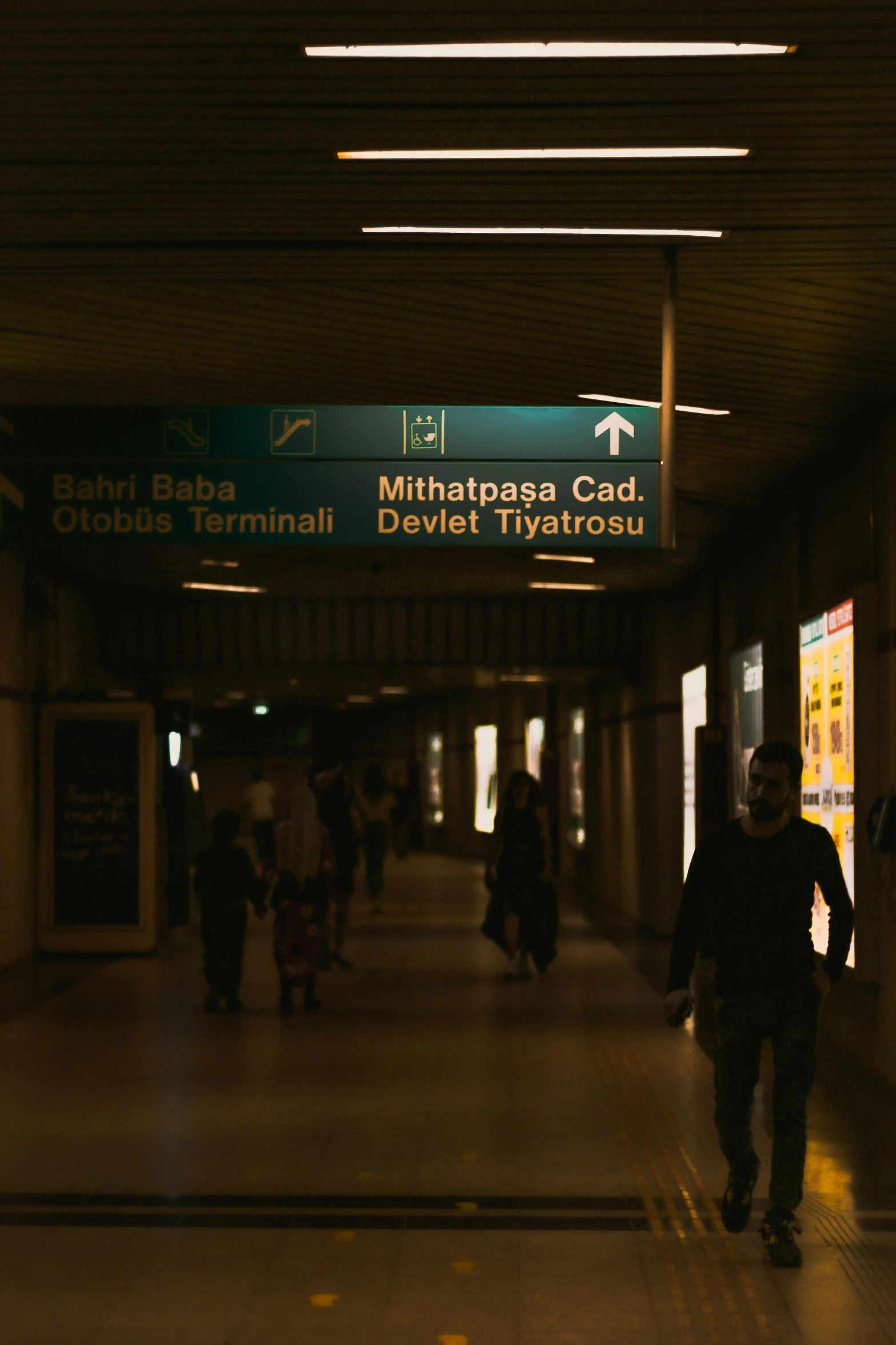 a group of people walking down a hallway, a poster, unsplash, hyperrealism, train station background, night light, signboards, hamar