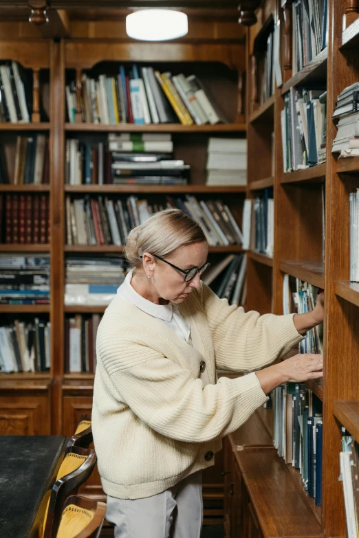 a woman is picking a book from a bookshelf, by Sara Saftleven, wearing white suit and glasses, russian academic, curated collections, a blond