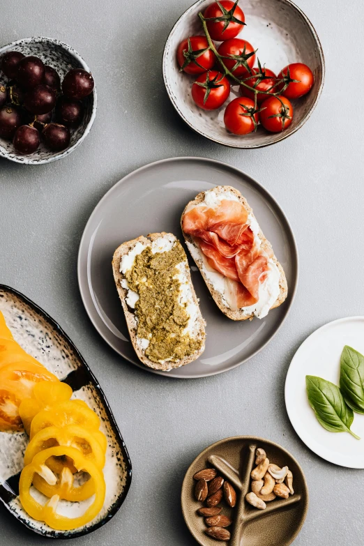 a table topped with plates of food and bowls of fruit, sandwich, lumi, grainy, mozzarella