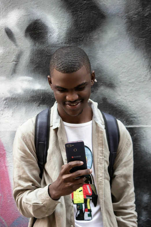 a man standing in front of a graffiti wall looking at his cell phone, a photo, happening, ( ( dark skin ) ), lgbtq, smiling for the camera, dark. no text