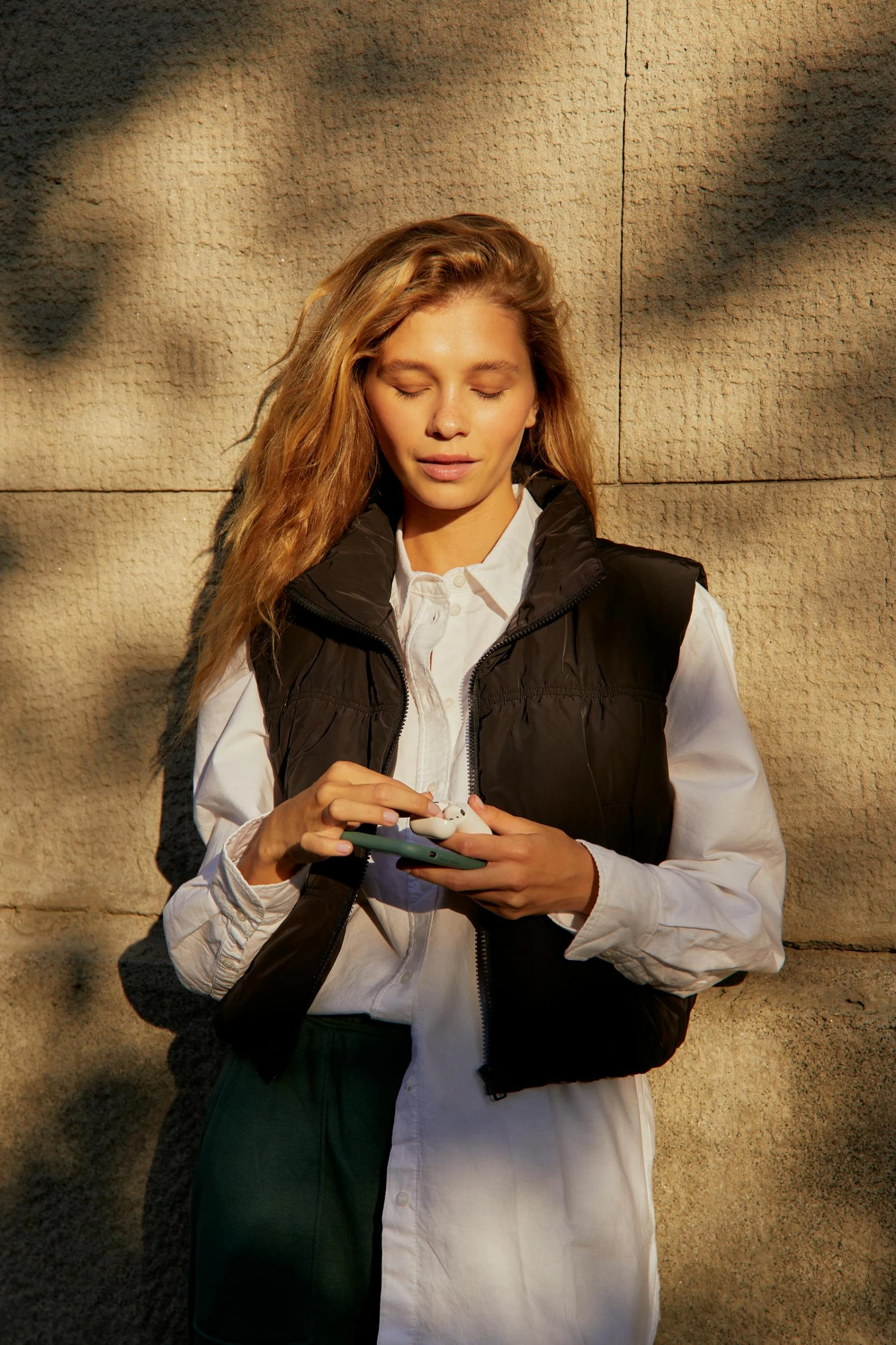 a woman standing in front of a wall using a cell phone, inspired by Emma Andijewska, renaissance, model is wearing techtical vest, nina agdal, cozy, utility