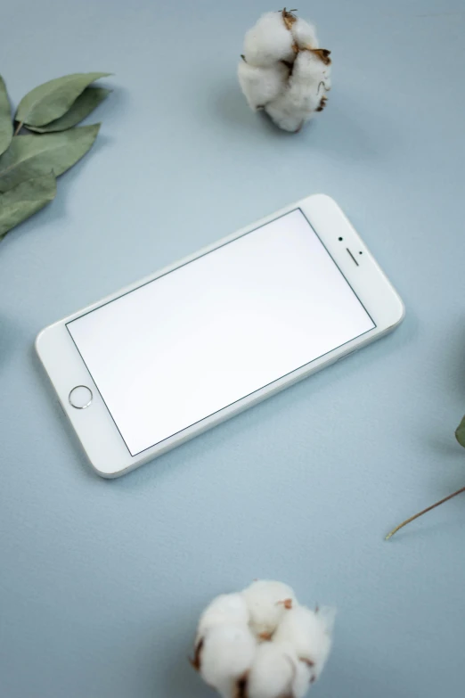 a cell phone sitting on top of a table next to a bunch of flowers, a picture, white and pale blue, item, device, no - text no - logo