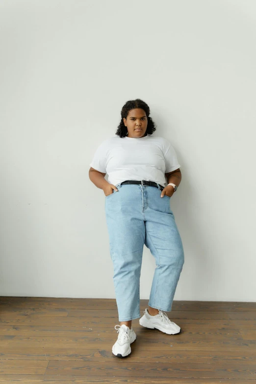 a woman standing against a white wall wearing high waisted jeans
