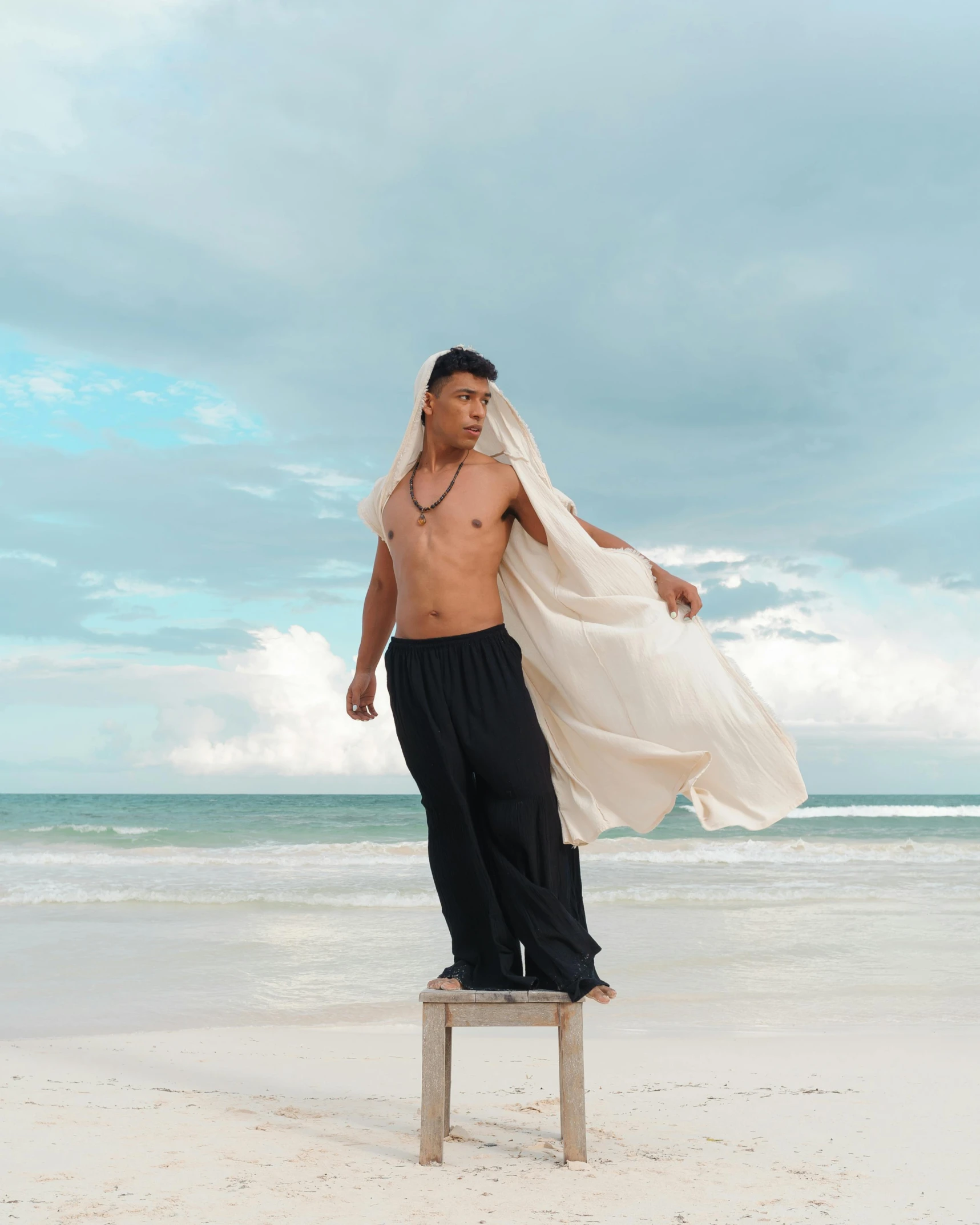 a man standing on top of a chair on a beach, an album cover, inspired by Byron Galvez, unsplash, sumatraism, white loincloth, wearing long gown, lgbt, model posing