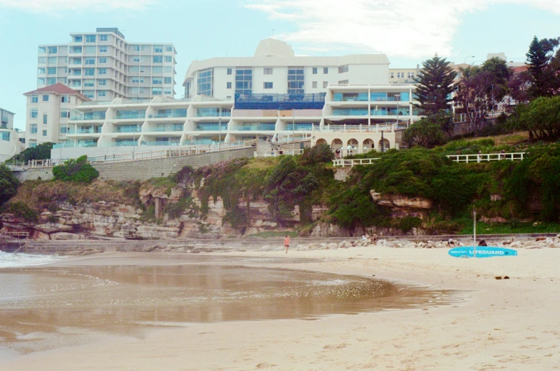 a beach with people walking around and a very tall building on the hill