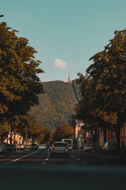 a street filled with lots of trees next to tall buildings, a picture, pexels contest winner, carpathian mountains, late summer evening, with a castle in the background, square