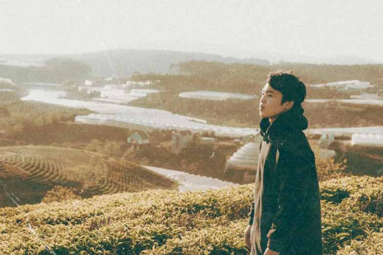 a man standing on top of a lush green hillside, an album cover, inspired by Kim Eung-hwan, unsplash, shin hanga, faded color film, japanese live-action movie, profile pic, beautiful boy