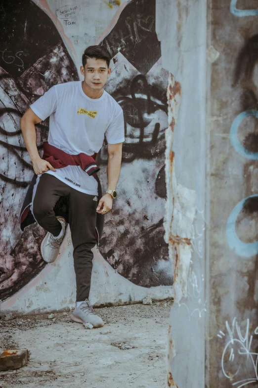 man in white shirt and red pants standing next to graffiti wall