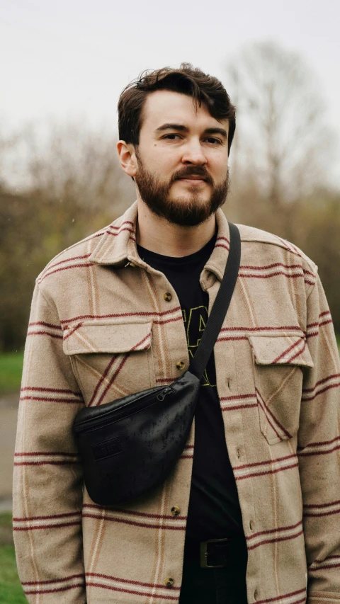 a man standing on top of a lush green field, an album cover, by Jessie Alexandra Dick, unsplash, wearing a plaid shirt, holding a gold bag, portrait of ricky gervais, with two front pockets