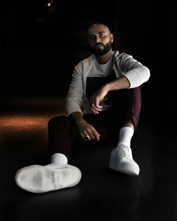 the man is posing on the floor near a pair of sneakers