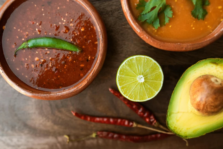 a wooden table topped with bowls of soup and an avocado, pexels, tachisme, holding hot sauce, background image, 🦩🪐🐞👩🏻🦳, quetzal and star-nosed mole