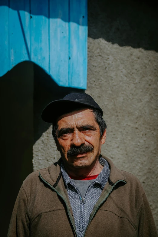 a man standing in front of a blue door, mexican mustache, bosnian, few wrinkles, the sun shines in