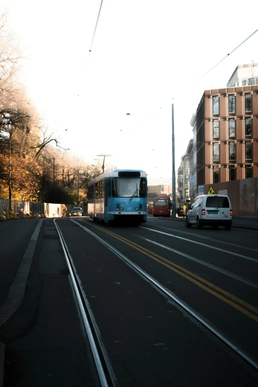 a blue bus driving down a street next to tall buildings, by Niko Henrichon, unsplash, viennese actionism, streets of heidelberg, trams ) ) ), low quality photo, winter sun