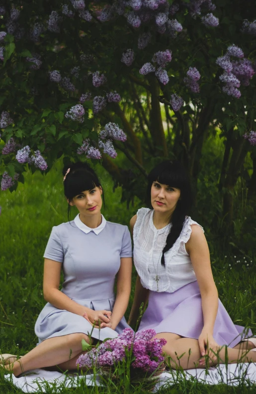 a couple of women sitting on top of a lush green field, an album cover, by Lucia Peka, pexels, purism, lilac bushes, portrait n - 9, low quality photo, ukrainian