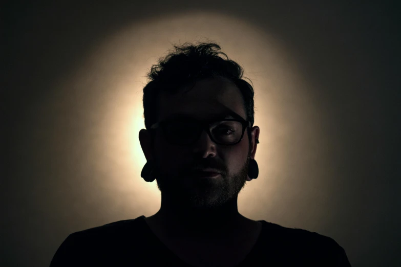 a man with glasses and a beard in a dark room, pexels contest winner, light and space, backlit ears, avatar image, male with halo, low quality photo