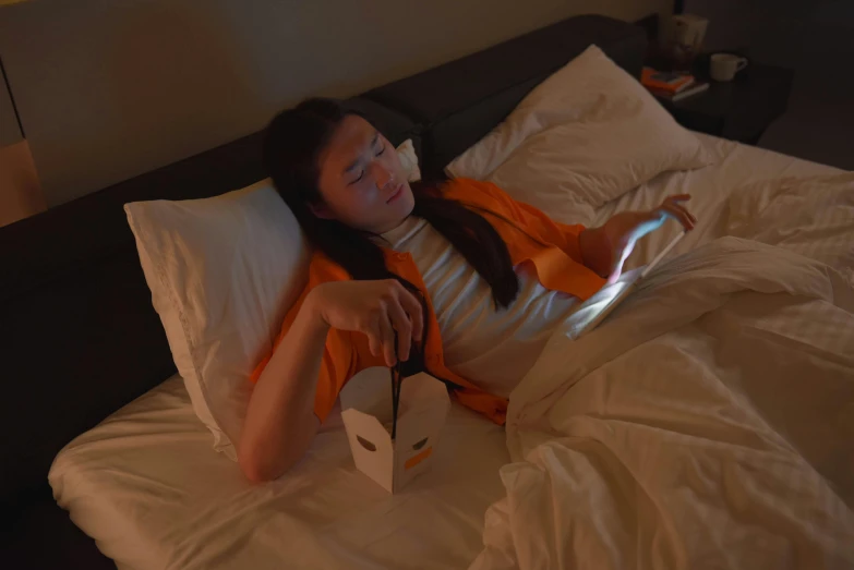 a woman laying in bed using a laptop computer, by Fei Danxu, happening, orange halo around her head, using a magical tablet, candid photograph, eating noodles