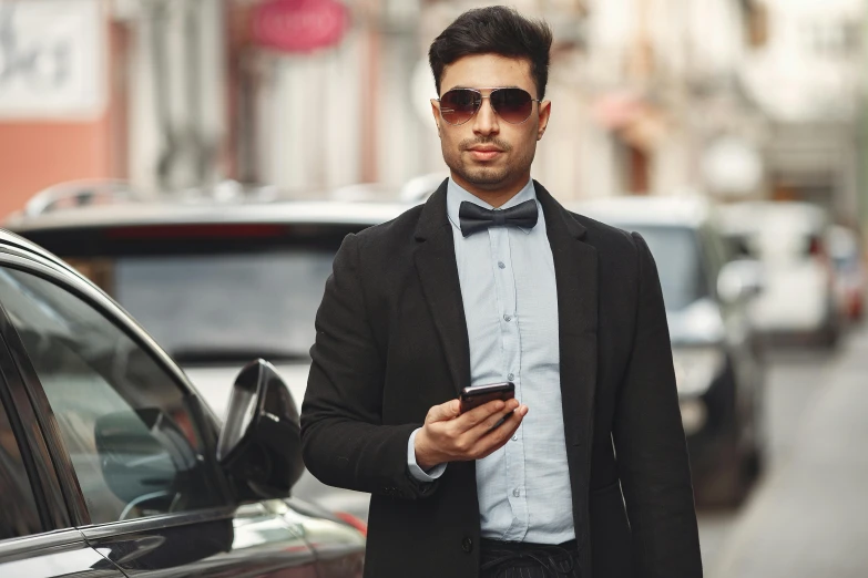 a man in a black bow tie stands in front of a car