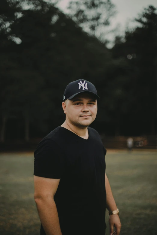 a man standing on top of a lush green field, an album cover, pexels contest winner, wearing baseball cap, headshot profile picture, alex flores, dark. no text