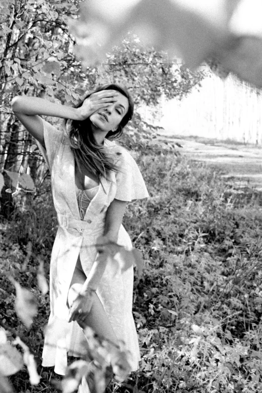 a woman in a dress standing in a field with her hand on her head