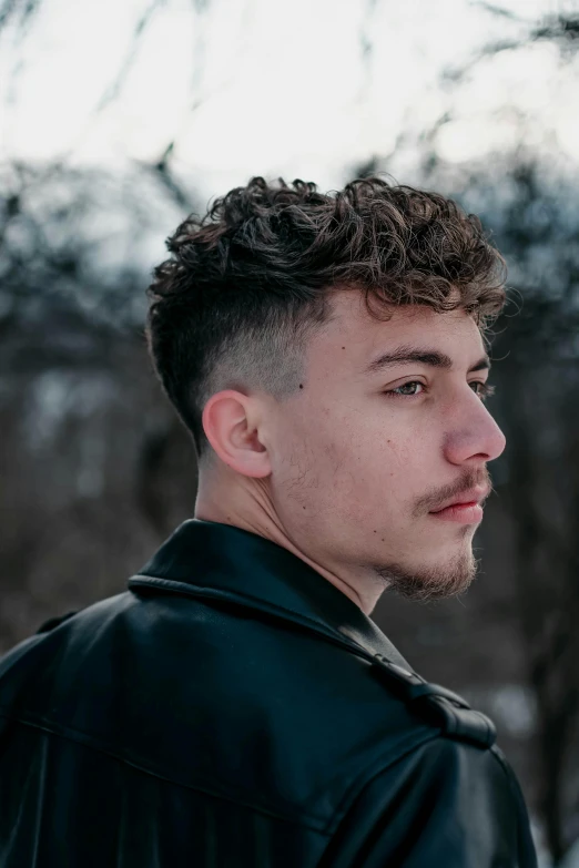 a man in a black jacket standing in the snow, an album cover, inspired by John Luke, trending on pexels, renaissance, headshot profile picture, shaved, curls, ignant