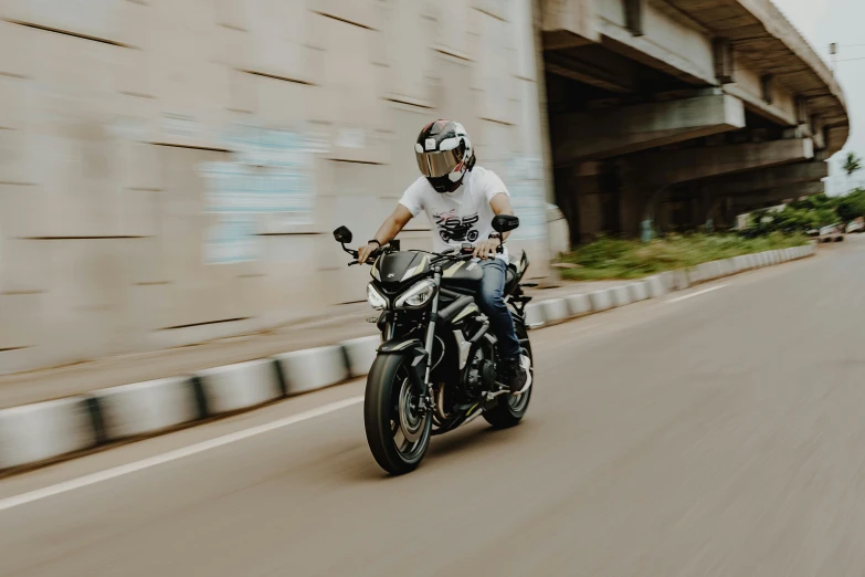 man on motorcycle speeding past an overpass and a large building