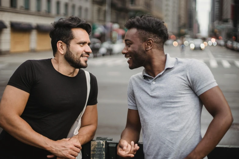 two men standing next to each other on a city street, trending on pexels, smiling at each other, gay, background image, brown skin man with a giant grin