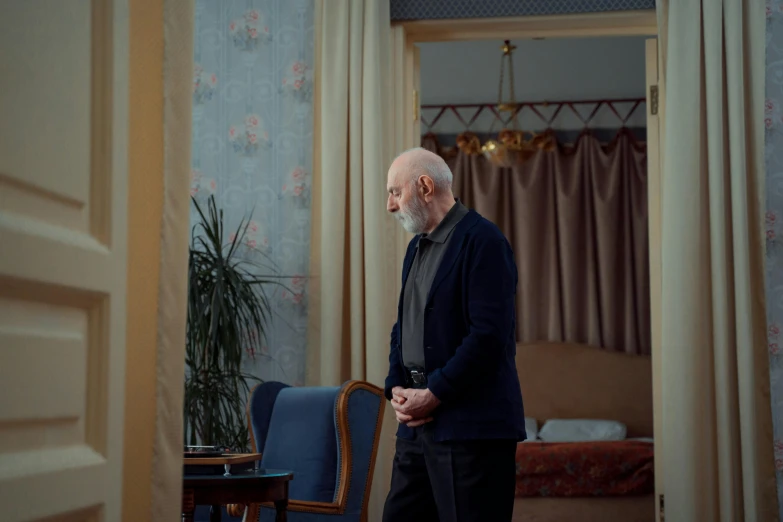 an older man in black jacket standing in front of a chair