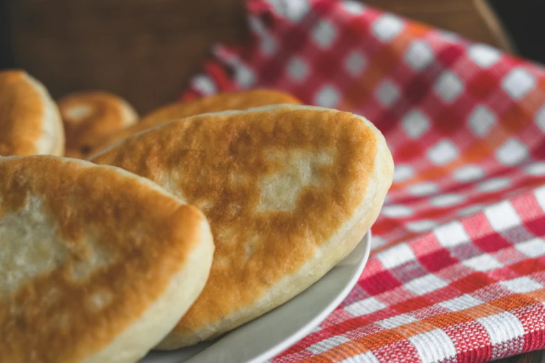 a plate of bread sitting on top of a red and white checkered napkin, inspired by Géza Dósa, unsplash, mingei, flat pancake head, 3 doors, eastern european, soft oval face