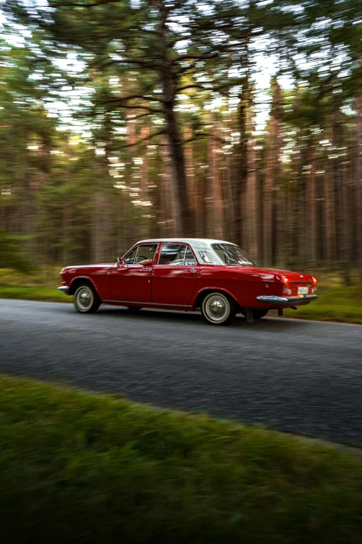 the classic car is driving along the road through the woods