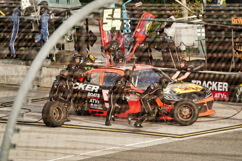 a group of men working on a race car, by Bertram Brooker, pexels contest winner, black and yellow and red scheme, exterior shot, stuck, nascar