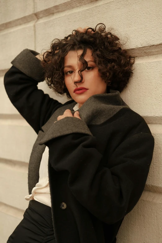 a woman leaning against a wall with her hand on her head, an album cover, by Winona Nelson, trending on pexels, renaissance, short coat, (dark shorter curly hair), style of paolo parente, thick collar