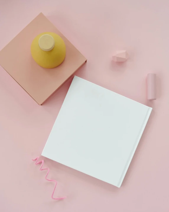 a book sitting on top of a table next to a cup of coffee, an album cover, inspired by Eden Box, unsplash contest winner, postminimalism, white and light-pink outfit, camera looking down upon, solid coloured shapes, white and yellow scheme