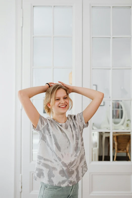 a woman standing in a room with her hands on her head, blonde swedish woman, wearing a t-shirt, smiling playfully, flowy