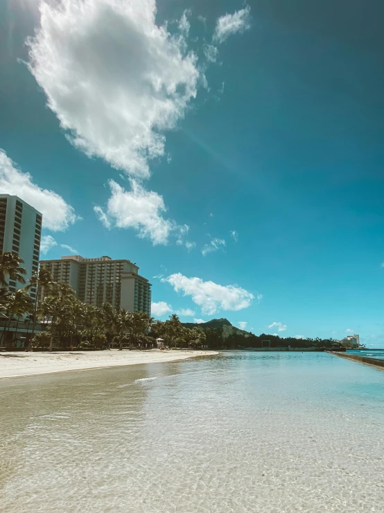 a large body of water sitting on top of a sandy beach, posing in waikiki, body of water, high rises, clear blue skies