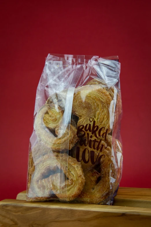 a bag of cookies sitting on top of a wooden table, inspired by Sarah Lucas, art brut, red swirls, on clear background, breads, vine twist