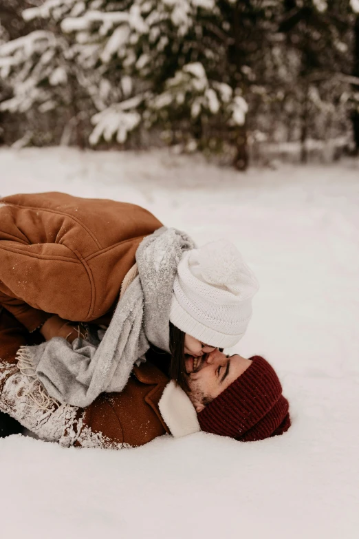 a person laying on the ground in the snow, by Anna Haifisch, pexels contest winner, romanticism, kissing together cutely, beanie, gif, maroon