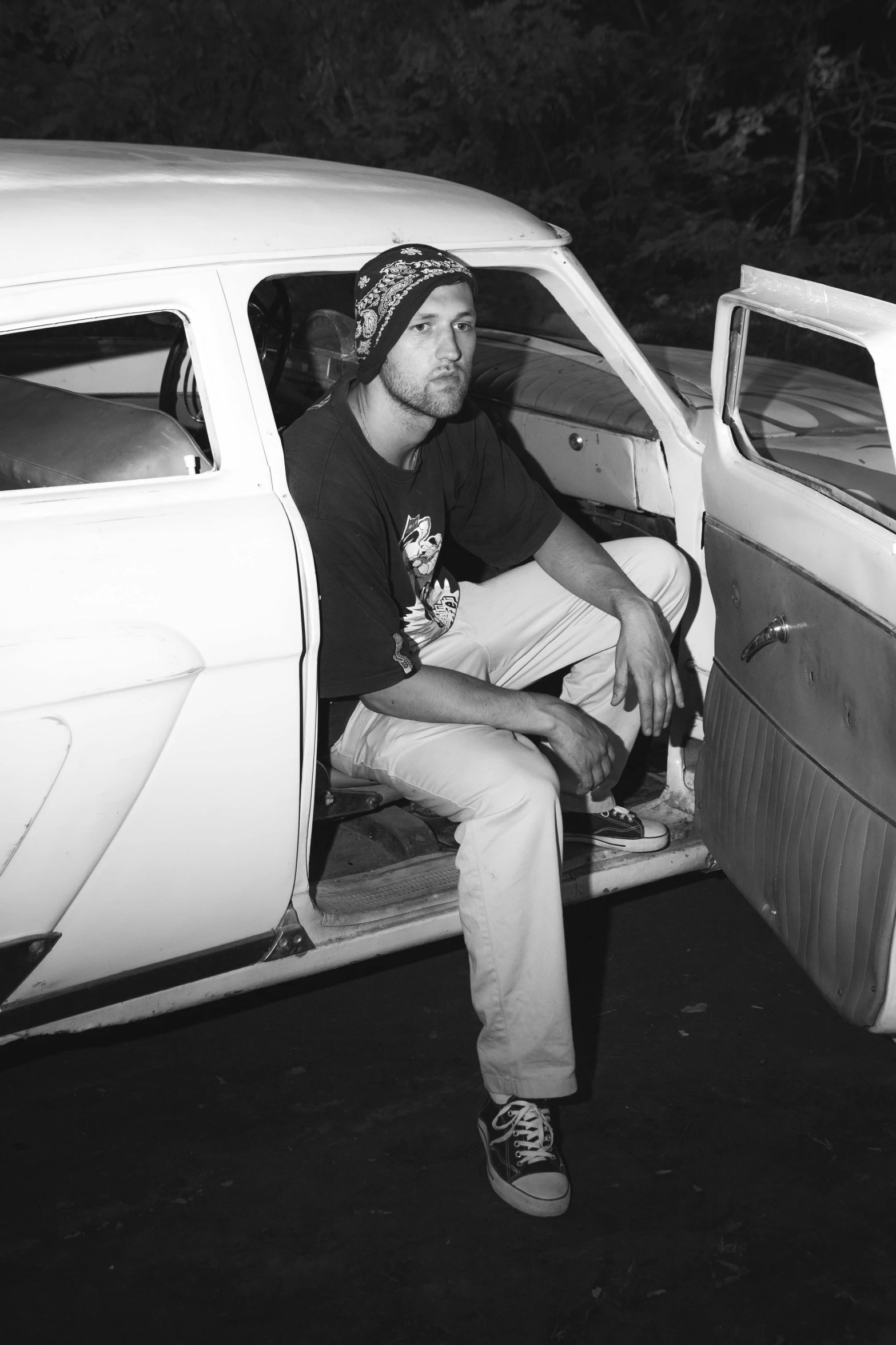 a black and white photo of a man sitting in a car, a black and white photo, happening, zachary corzine, hippy, dingy, structure : kyle lambert